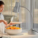 A woman using an Avantco stainless steel heat lamp to serve food from a bowl on a table.