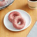 Two Southern Roots red velvet cake donuts on a plate next to a cup of coffee.