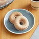 Two Southern Roots vegan original glazed cake donuts on a plate next to a cup of coffee.