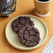 A plate with two Southern Roots double chocolate chip cookies next to a cup of coffee.