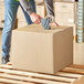 A person holding a Lavex Kraft cardboard shipping box.