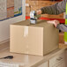 A person using a tape dispenser to seal a Lavex cardboard shipping box.