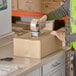 A person in a safety vest using a box cutter to open a Lavex cardboard shipping box.