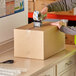 A man in a safety vest using a box cutter to pack a Lavex cardboard shipping box.