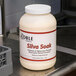 A white bottle of Noble Chemical Silva Soak tableware presoak powder on a metal surface.
