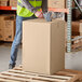A man wearing a safety vest and holding a Lavex Kraft corrugated shipping box.