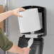 A person putting a white Tork Advanced paper towel roll into a dispenser.