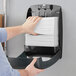 A hand putting Tork Advanced white multi-fold paper towels into a dispenser.