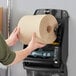 A person holding a Tork Natural Kraft paper towel roll in front of a paper towel dispenser.