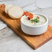 A bowl of Chef's Companion cream soup with bacon and bread on a wooden cutting board.