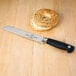 A Mercer Culinary bread knife next to a bagel on a table.