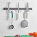 A Choice 24" Magnetic Knife Holder with kitchen utensils and knives on a wall.