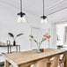 A dining table with Canarm Declan matte black pendant lights above it and a vase of flowers.