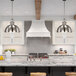 A Canarm Polo brushed nickel pendant light hanging over a kitchen island with bar stools.