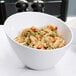 An American Metalcraft white melamine serving bowl filled with pasta and vegetables on a table.
