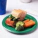A sandwich on a Creative Converting emerald green plastic plate with broccoli and carrots.