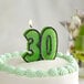 A white birthday cake with a lit green glitter "30" candle.