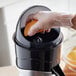 A gloved hand squeezing an orange into a Galaxy CJ180 electric citrus juicer on a counter.