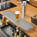 A Regency stainless steel beer drip tray on a bar counter with a glass of beer.