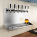 A Regency stainless steel wall mount beer dispenser with a glass of beer.