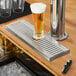 A Regency stainless steel surface mount beer drip tray on a bar counter with a glass of beer on it.