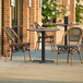 A Lancaster Table and Seating round Yukon oak table with two brown French bistro chairs on an outdoor patio.