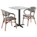 A Lancaster Table & Seating Versilla table with 2 French bistro chairs with black and white seats.
