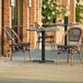 A Lancaster Table & Seating Paladina table with 2 black French bistro chairs on an outdoor patio.