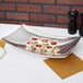 A Vollrath stainless steel curved platter with food on it sits on a table.