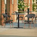 A Lancaster Table & Seating round table with 2 black French bistro chairs on a patio.
