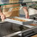 A full size stainless steel food pan filled with cooked food being placed in a buffet or food service station.