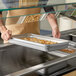 A full size heavy weight chafer food pan filled with cooked food being placed in a serving station.