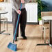 A man using a Lavex angled broom with a blue flagged bristles and a metal handle to sweep the floor.