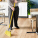 A man using a Lavex angled broom with a yellow flag to sweep the floor in a corporate cafeteria.