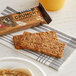 A package of Kodiak Cakes Peanut Butter Crunchy Granola Bars on a table with a snack bar and a glass of orange juice.