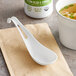 A white World Centric compostable Asian soup spoon on a napkin next to a bowl of soup.