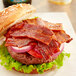 A close up of a bacon burger with lettuce and tomato.