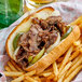 A plate with a sandwich made with Original Philly Cheesesteak Co. Wow Seasoned Beef Steaks, onions, and fries.