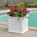 A white Mayne Cape Cod planter with a potted plant with pink flowers in it.