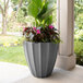 A Mayne graphite gray planter with pink and green flowers in it.