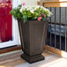 An espresso Mayne Aberdeen planter with flowers on an outdoor patio table.