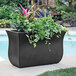 A Mayne black trough planter with plants on a outdoor patio table.