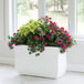 A white Mayne Valencia trough planter with flowers in it.