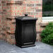A black rectangular Mayne Mansfield storage bin with a square top next to a brick wall.