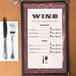 An 8 1/2" x 14" burgundy marble border menu on a table with a wine list and silverware.