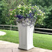 A white Mayne Cambridge planter with colorful flowers.