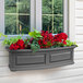 A Mayne Nantucket window box with red flowers and plants on an outdoor patio counter.