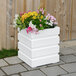 A white square Mayne Freeport planter with colorful flowers.