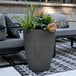 A Mayne graphite gray planter with flowers on a table on an outdoor patio.