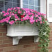A white planter box with pink flowers on a brick wall.